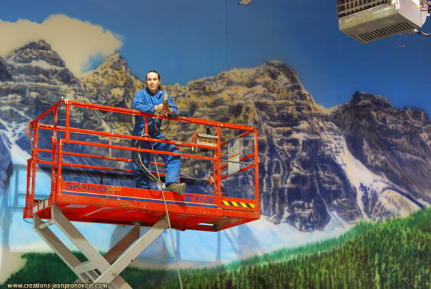 Airbrush painter artist Jean Pronovost in front a large scale mural